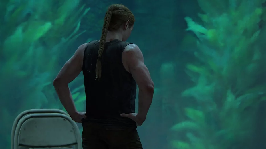 Abby stands with her hands on her hips against the green-blue tank of the aquarium