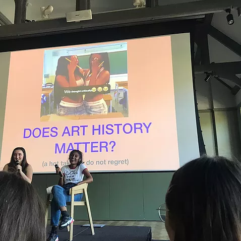 zarina and gabrielle are on stools on a stage and behind them is a huge projection saying &lsquo;does art history matter?'