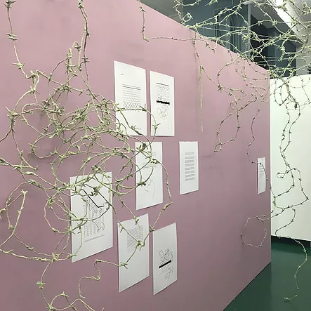 a pink wall with white pieces of paper stuck to it and barbed wire in white all over the front of the wall framing the paper