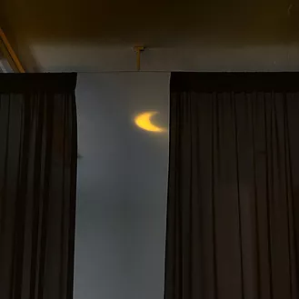 between the gap in the curtains, a small crescent yellow moon is projectod onto the wall up high and barely visible