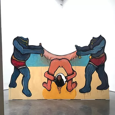 there&rsquo;s a big drawing or painting on a wooden board where the viewer can put their heads on top of the figures or in a hole to become a part of the scene. The scene is two headless figures holding the edges of a saw and passing it back and forth cutting into a person in the middle who is bent over and showing us their bum