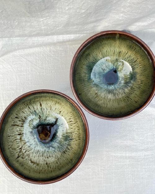 we are looking down into two bowls that have a design inside lmost like pupils, with a dark spot in the centre flecking outwards into a light green yellow spray