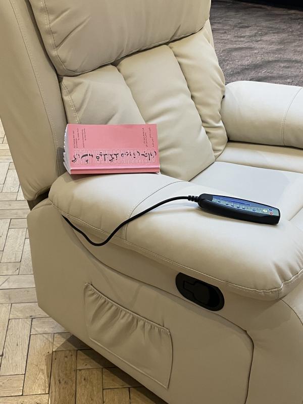 close up of the beige leather massage chair. The little remote is resting on the arm, next to a pink exhibition publication