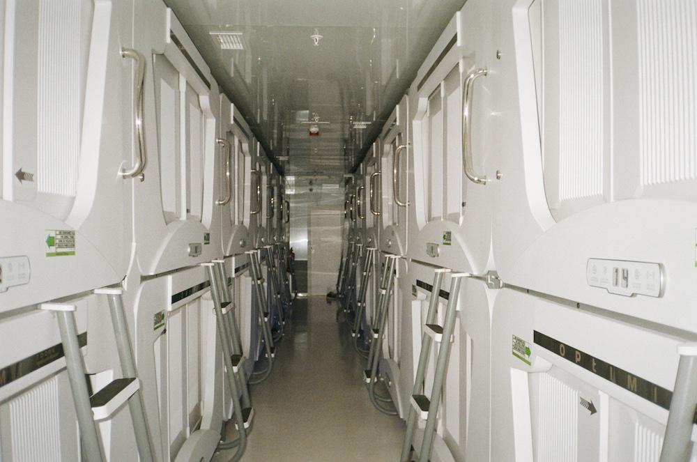 film photograph of a capsule hotel showing a corridor between bunks