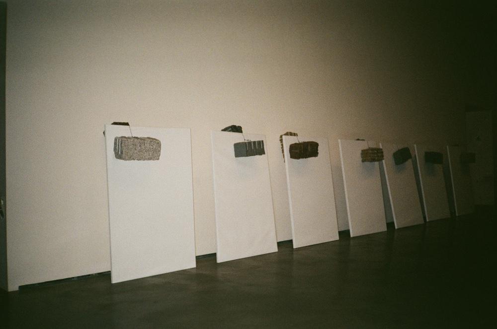 Giovanni Anselmo's Untitled piece from 1984 showign canvases leaning against a wall, with rocks balancing over the top