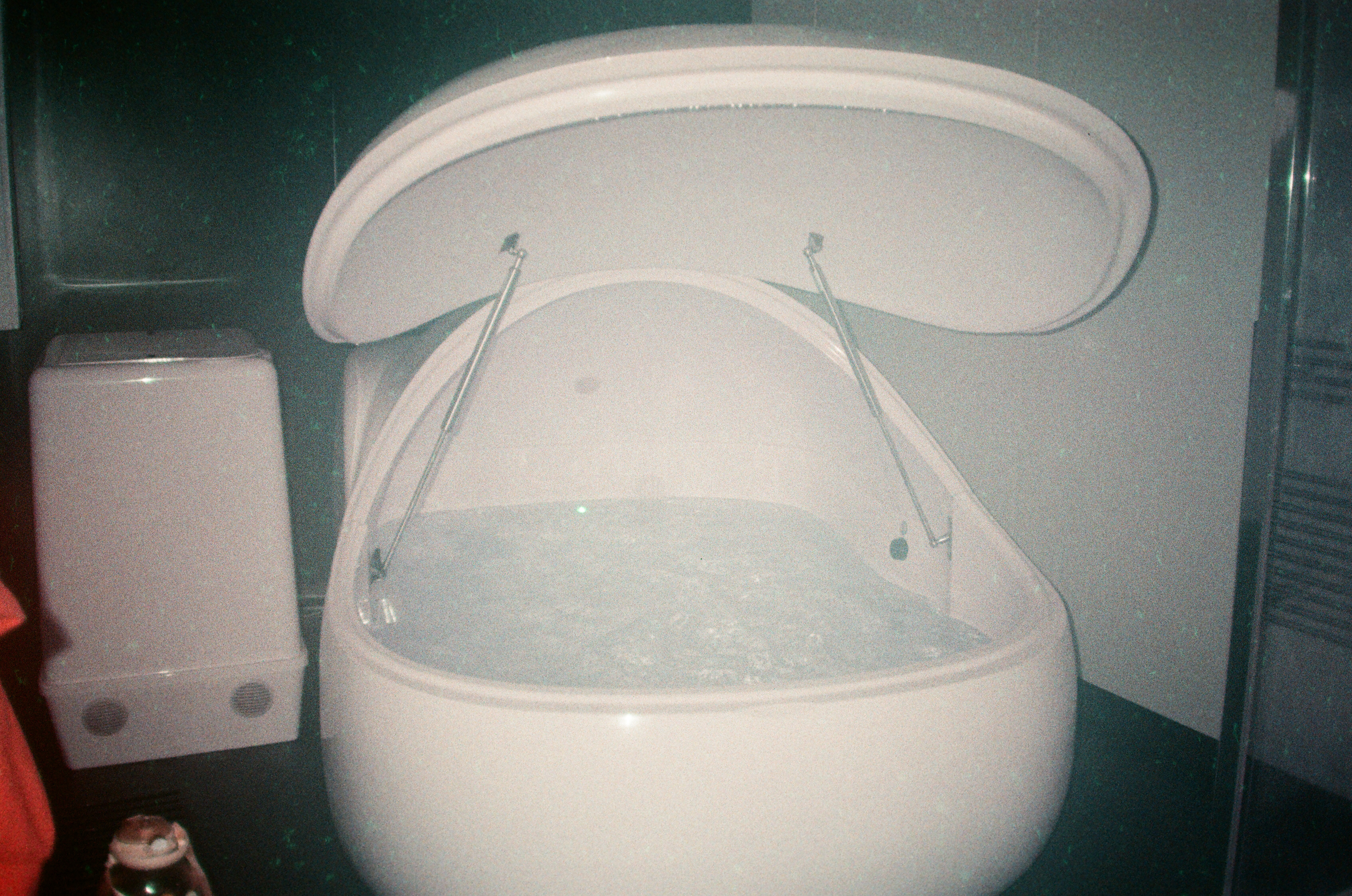 a grainy film photography of a big smooth white floatation tank that is open and showing clear water inside