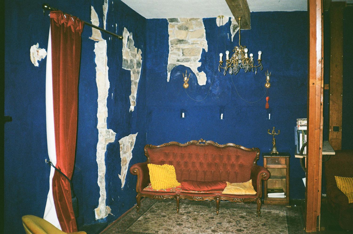 blue painted onto the wall, although some cracks showing bricks have been left exposed. in front, a chandelier, a red curtain, and a red deep button low sofa